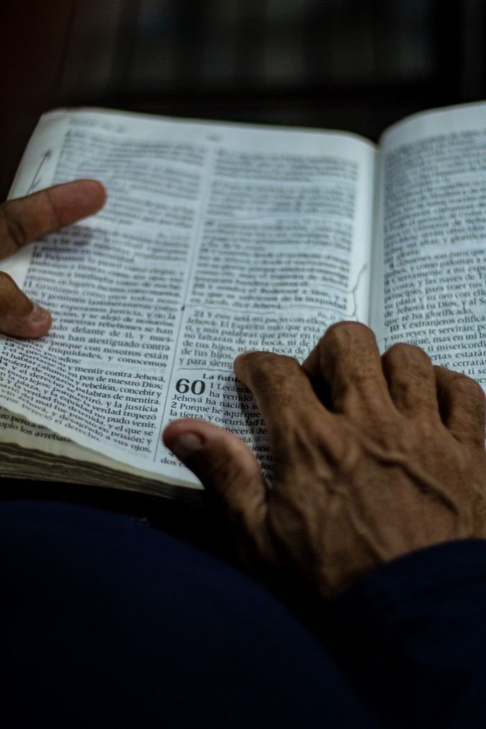 A close-up of elderly hands holding and reading an open book in dim lighting, conveying wisdom and focus.