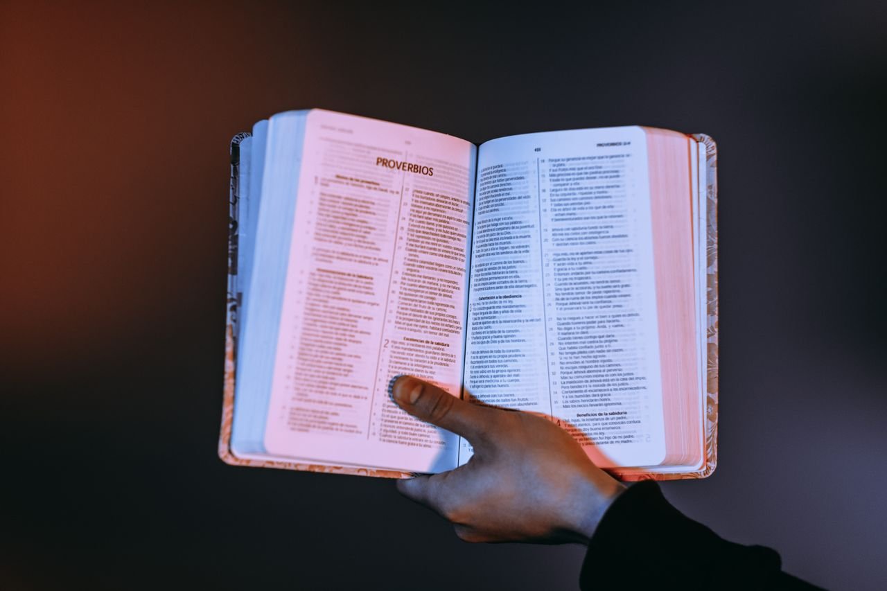 about-01 A person holds an open Bible with Proverbs highlighted, bathed in warm light.