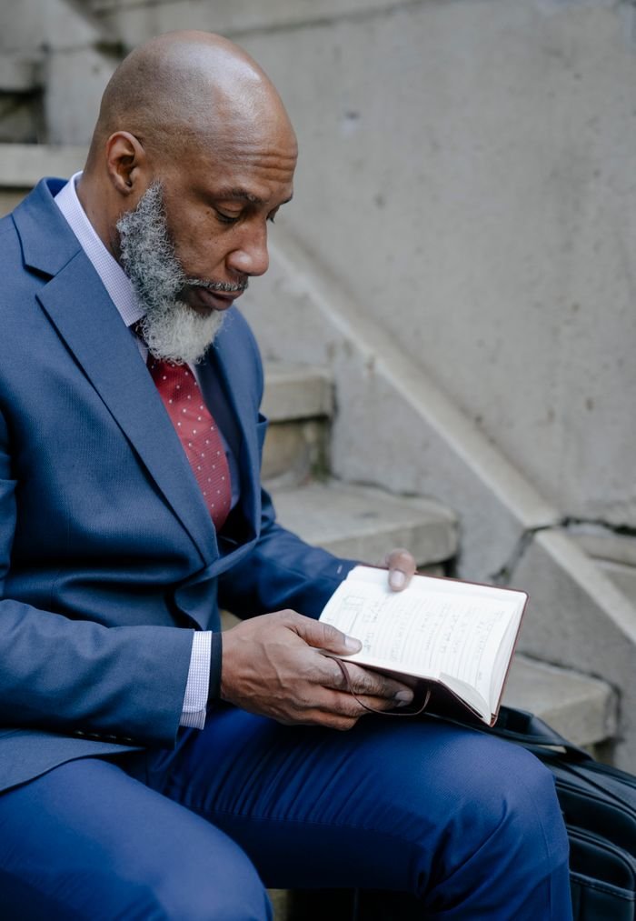 Senior man in a blue suit reading on stairs, exuding wisdom and sophistication.