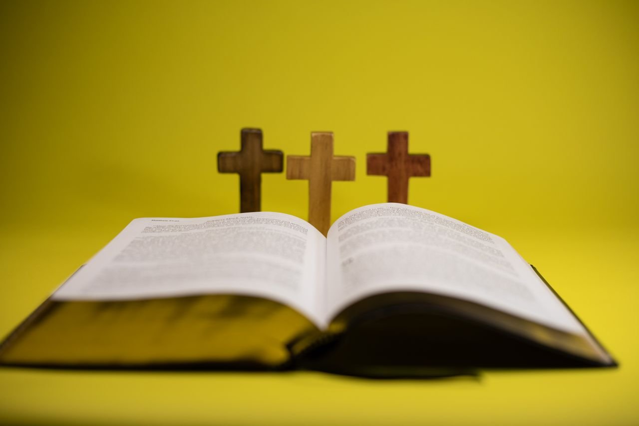 impact-img An open Bible with three crosses displayed against a vibrant yellow backdrop.